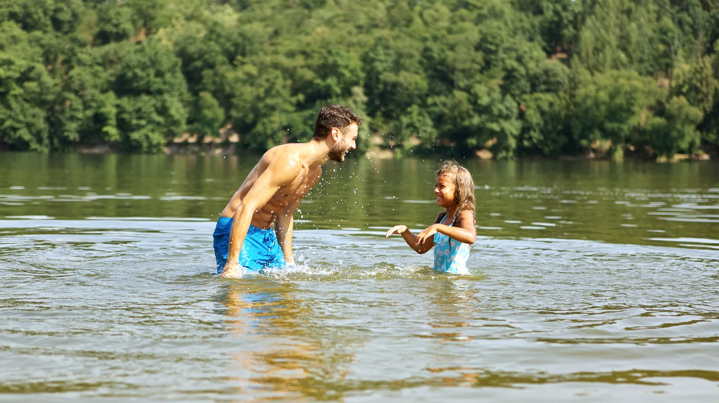 Een vader staat dichtbij zijn dochter in het water en begeleidt haar spelend